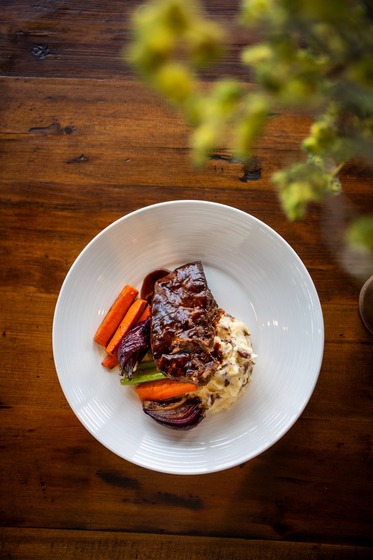 Braised beef over creamy mashed potatoes with roasted carrots and onions in a white bowl